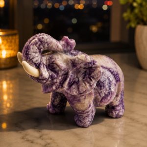 Natural hand-carved Amethyst crystal elephant statue with an upward-raised trunk, polished purple gemstone finish, displayed on a marble surface with a soft blurred background.